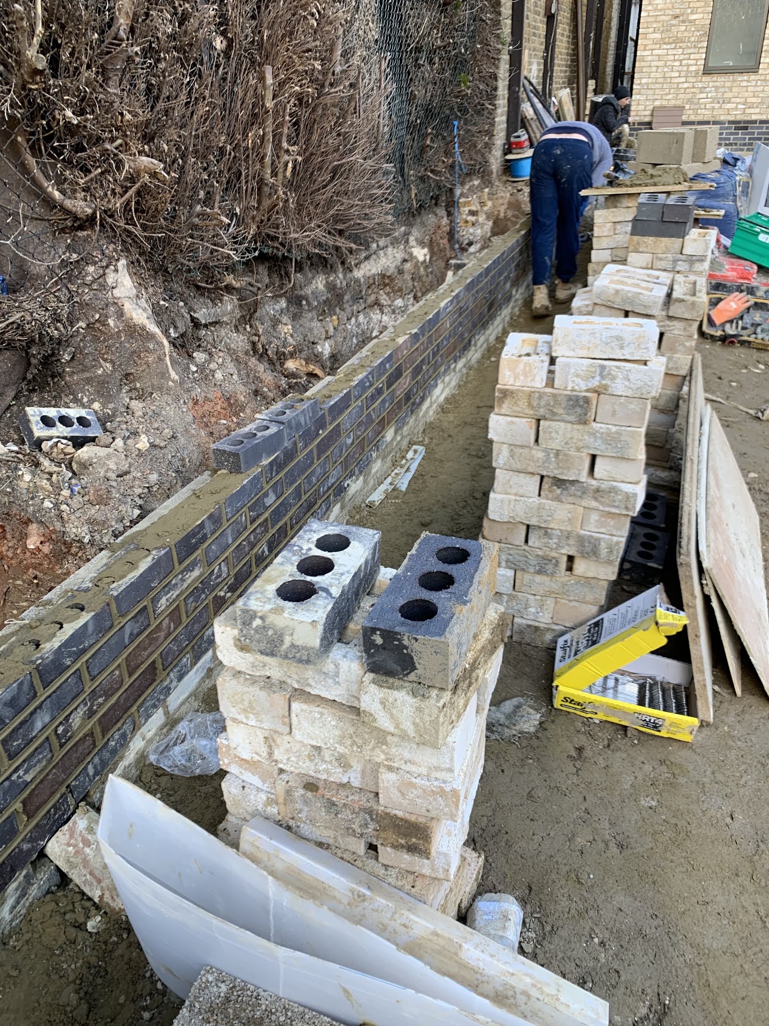 A retaining wall going up in blue brick against a bank